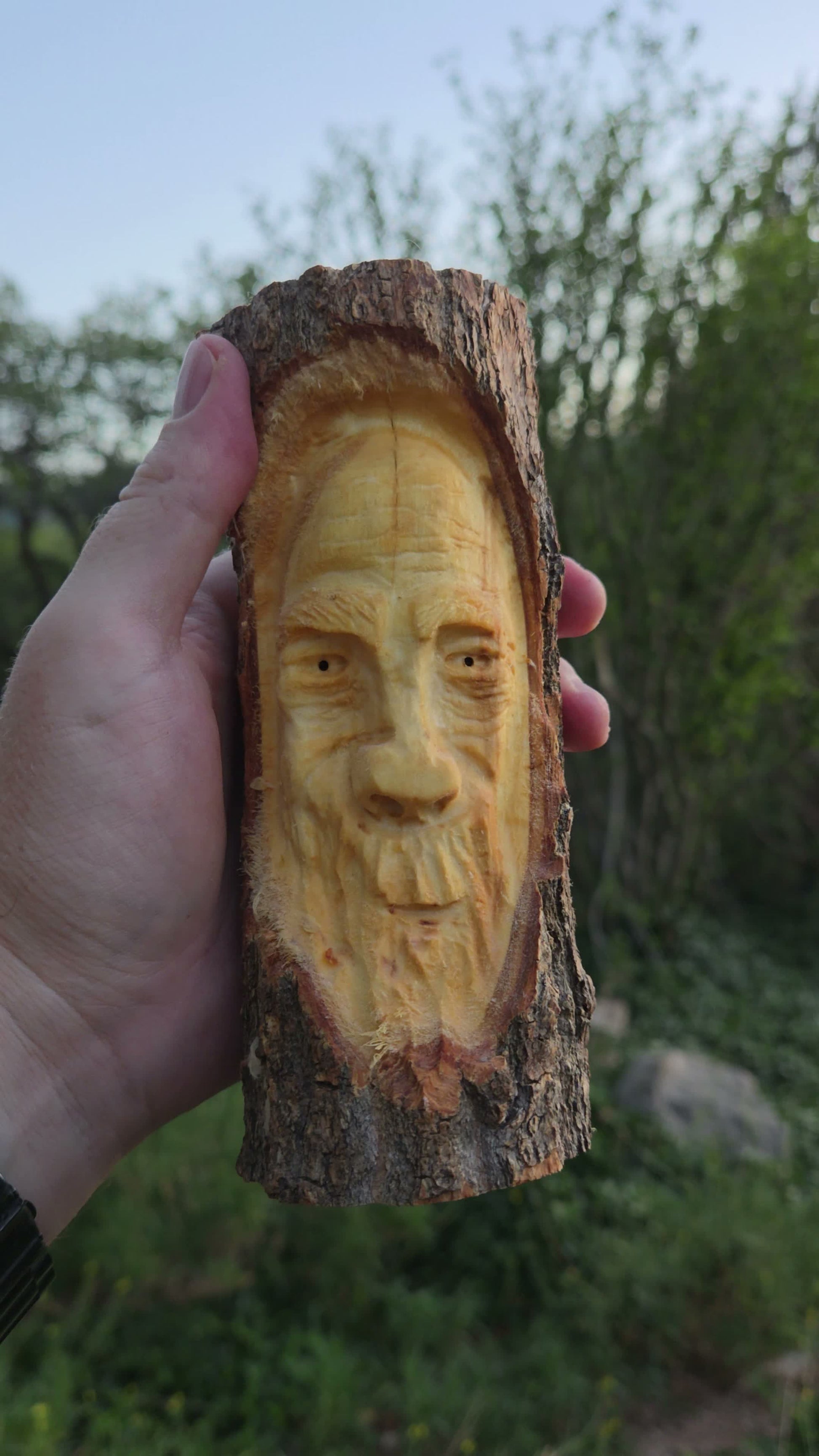 Hand-carved cottonwood wood spirit with half-closed eyes and split beard inside an oval bark opening, held in hand in New Mexico